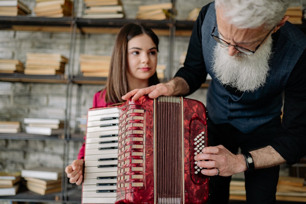 An elderly man instructing a teenage girl on playing an accordion. Perfect for education or music themes.