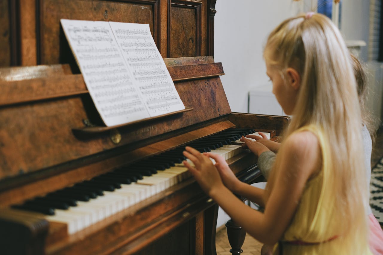 Two young girls playing piano together indoors, focused on a music sheet.