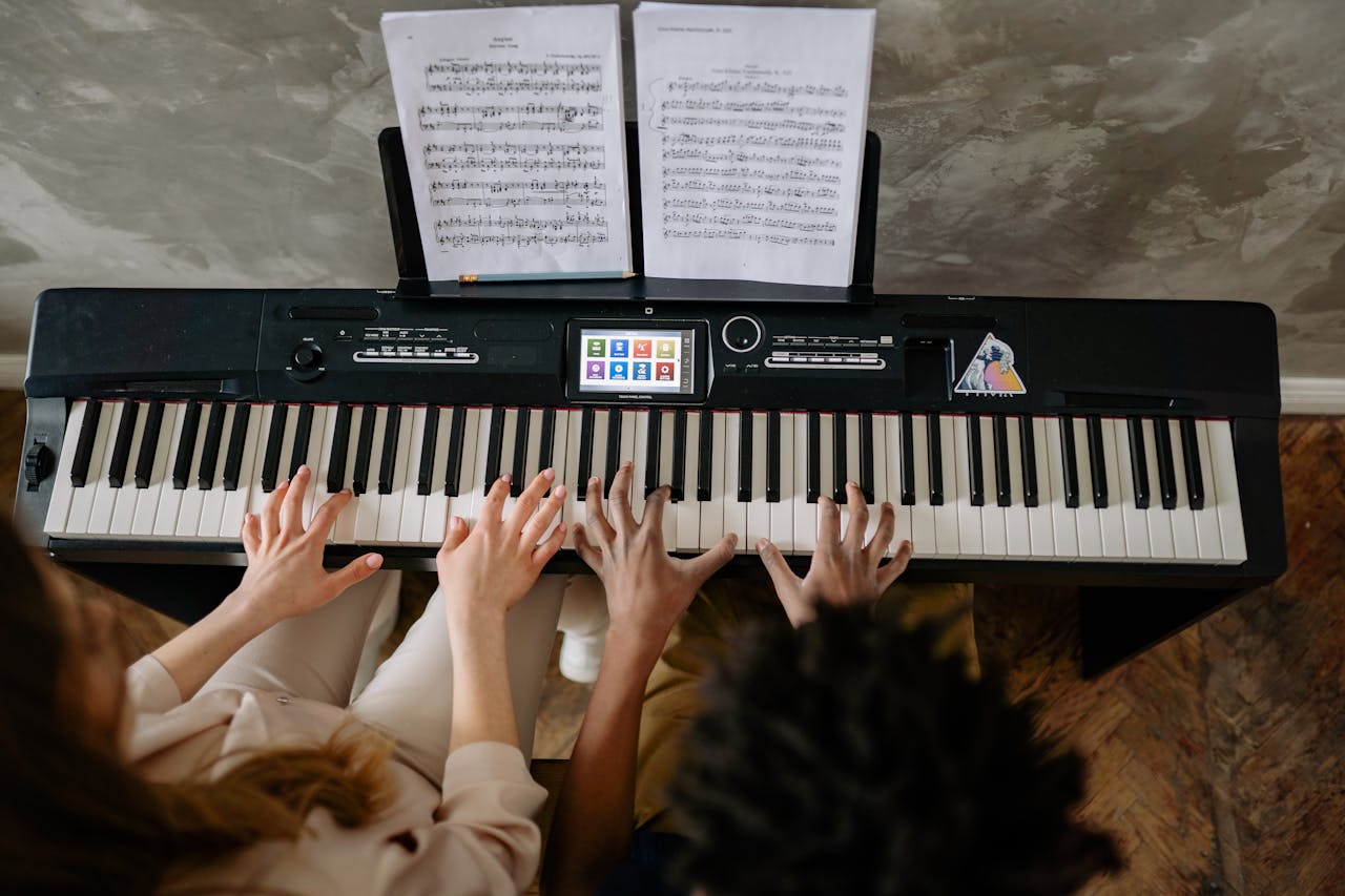 Teacher and student playing piano together for a hands-on learning experience.