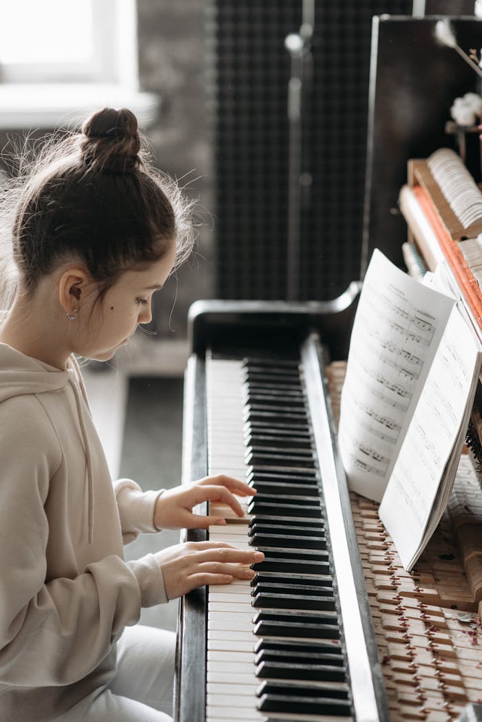 A young girl practicing piano indoors, focusing on sheet music beside her.